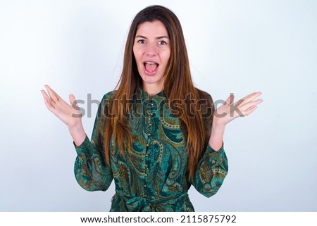 Surprised terrified Young caucasian woman wearing floral dress over white background Gestures with uncertainty, stares at camera, puzzled as doesn't know answer on tricky question, People, 