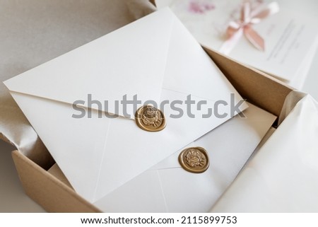 White envelopes sealed with golden floral wax stamp, luxury stationery packed in a box and ready to mail