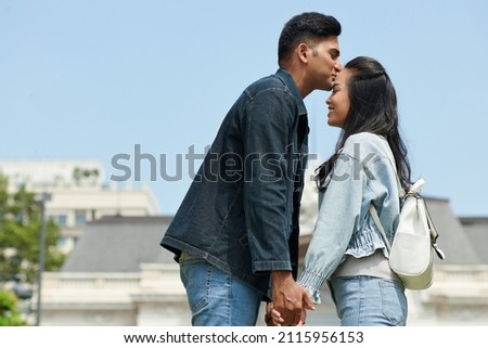 Young man kissing his smiling girlfriend on forehead with love and tender when they are standing outdoors Royalty-Free Stock Photo #2115956153