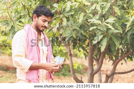 happy young indian former counting money at farm land - concept of successful forming business, agricultural profit and finance. Royalty-Free Stock Photo #2115957818