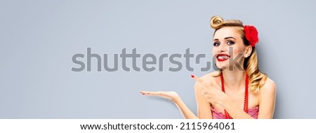 Portrait photo of excited happy smiling beautiful woman pointing away side with index finger over grey background. Pin up girl showing, giving, hold, demonstrate promote some product or slogan ad text