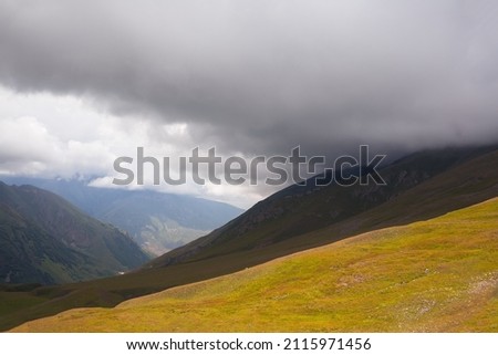 A large thundercloud covers the mountain valley. Soft focus on a hillside. Wide angle photography.