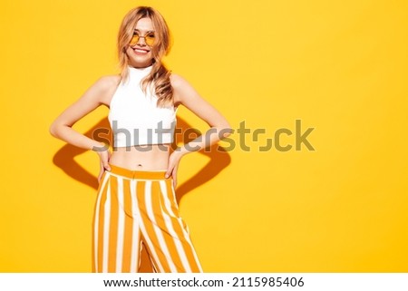 Portrait of young beautiful smiling blond female in trendy summer clothes. carefree woman posing near yellow wall in studio. Positive model having fun indoors. Cheerful and happy Royalty-Free Stock Photo #2115985406