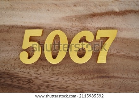 Wooden Arabic numerals 5067 painted in gold on a dark brown and white patterned plank background.