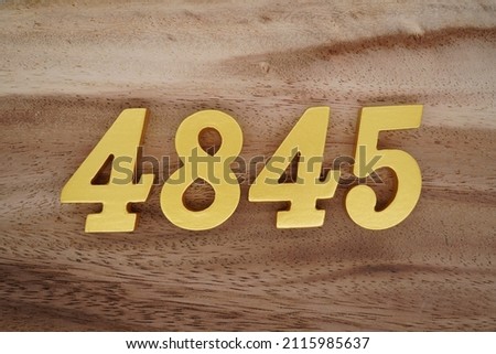Wooden Arabic numerals 4845 painted in gold on a dark brown and white patterned plank background.