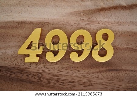 Wooden Arabic numerals 4998 painted in gold on a dark brown and white patterned plank background.