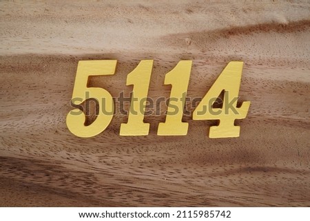 Wooden Arabic numerals 5114 painted in gold on a dark brown and white patterned plank background.