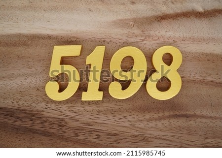 Wooden Arabic numerals 5198 painted in gold on a dark brown and white patterned plank background.