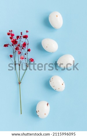 Easter minimal composition with eggs and flowers on the blue background. Easter concept. Vertical photo, flat lay.
