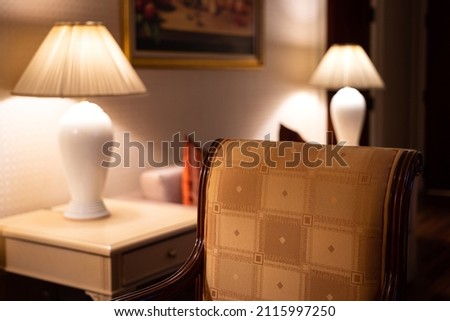 A classic style armchair in living room with glowing lantern as background. Interior decoration object photo. Selective focus at armchair textile surface. Photo contained noise due to low light.