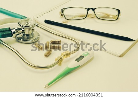 Stethoscope, thermometer, pills and a notebook with a pencil, glasses on the table of a doctor or nurse. Diagnosis and detection of viral disease COVID-19. Selective focus, blur background. Toned.