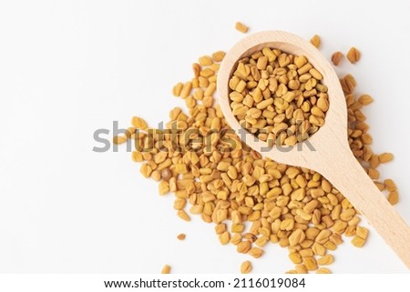 Macro photo of dry yellow fenugreek seeds or shambhala, helba seeds in wooden spoon on white background, top view Royalty-Free Stock Photo #2116019084