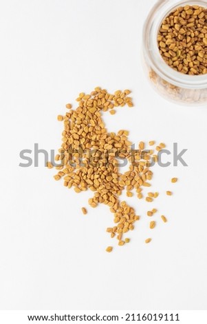 Scattered yellow fenugreek seeds or shambhala, helba seeds  on white background, top view Royalty-Free Stock Photo #2116019111