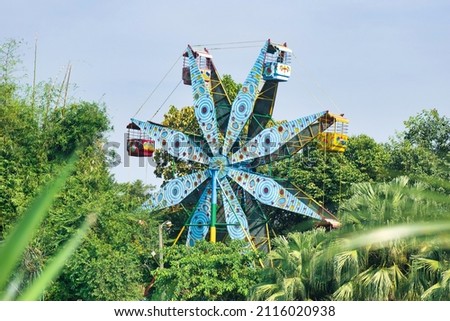 Ferris wheel in amusement park in Bangladesh.Green trees and mountain with blue sky.