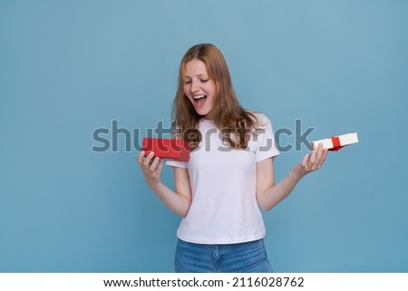 Surprised young caucasian woman holding red gift box and shocked with open mouth standing on blue background beautiful girl happy smile holding generic box suitable for any holiday Use for advertising