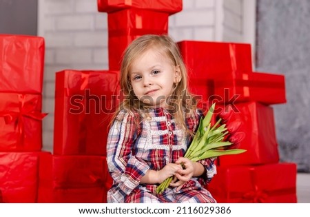 Adorable kid with a spring flower. Beautiful girl with flowers. Young blond girl celebrating her birthday at home. Portrait of a happy little girl. Romantic charming girl holds a bouquet of tulips.