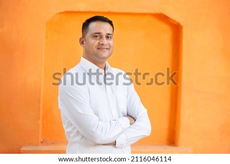 Confident young indian man wearing white shirt standing cross arms against orange background, Smiling handsome asian male with positive expression posing.