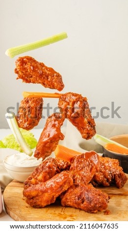 Falling chicken wings buffalo sauce with carrot and celery sticks. Fried bbq wings in flight. Traditional American cuisine concept. Royalty-Free Stock Photo #2116047635
