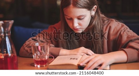 A cute teenage girl reading book in cafe. Education, leisure, hobby, back to school concept. Banner.
