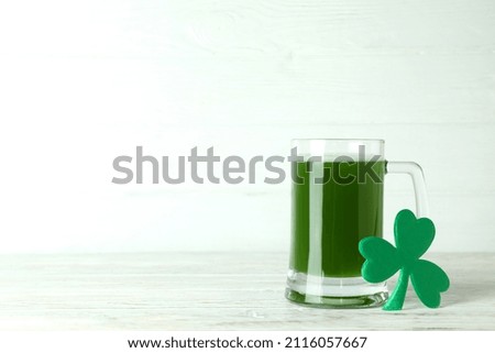Glass of ale and clover on wooden table, space for text