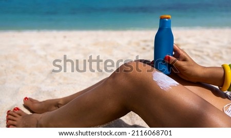Selective focus of sun cream on woman  legs with  sunscreen bottle on the sand beach as applying moisturizing lotion on .Skin care protection cpncept