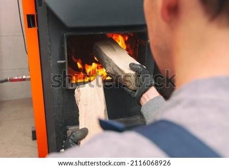 Man loads the firewood in the solid fuel boiler in the boiler room. Solid fuel and heating concept  Royalty-Free Stock Photo #2116068926
