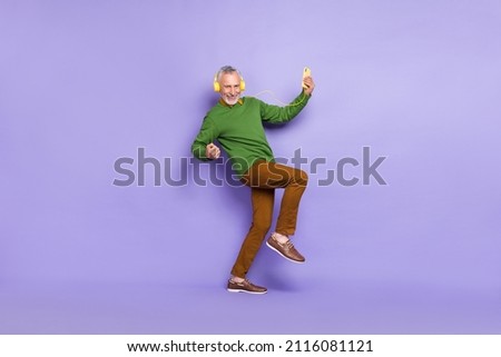 Photo of excited man pensioner dressed pullover dancing rising fists listening music gadget isolated purple color background
