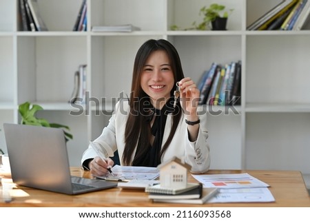 Real estate agent holding house key in hand and smiling at camera. Real estate investment and insurance concept.