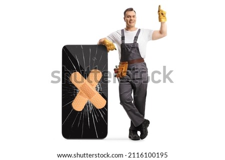 Full length portrait of a repairman leaning on a broken smartphone with bandage and pointing up isolated on white background Royalty-Free Stock Photo #2116100195