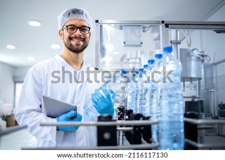Portrait of smiling caucasian technologist expert with tablet computer standing by automated machine for PET water production in bottling factory. Royalty-Free Stock Photo #2116117130