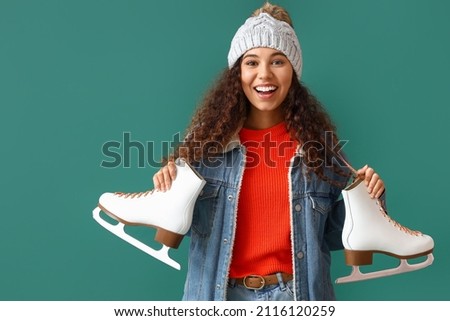 Beautiful young woman in winter clothes and with ice skates on color background