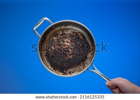Dirty oily burnt metal frying pan held in hand by male hand. Royalty-Free Stock Photo #2116125335