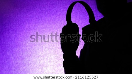 Silhouette Man holding headphones in his hands listening to music on a beautiful purple background. Musical background with a DJ with headphones in his hands, copy space