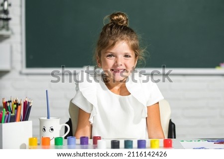 Little girls drawing a colorful pictures with pencil crayons in school classroom. Funny school girl face.