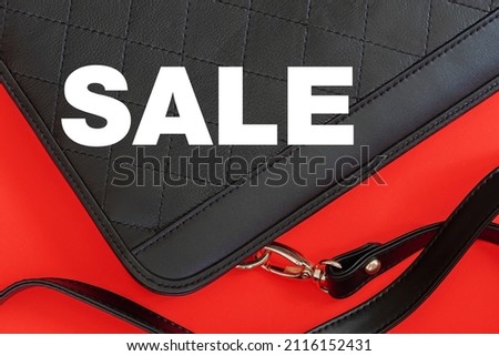 Word Sale on black leather handbag with stitching on a red bright ed background, top view, flat lay. Concept of shopping and seasonal discounts