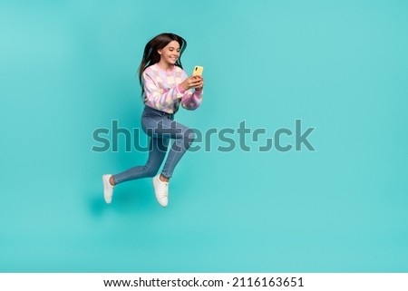 Full length body size view of pretty trendy cheery girl jumping using device chatting isolated on vivid teal turquoise color background