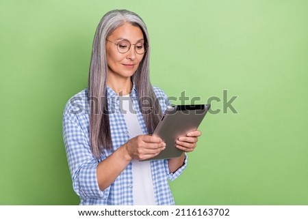 Photo of nice aged grey hairdo lady hold tablet wear spectacles plaid shirt isolated on green color background