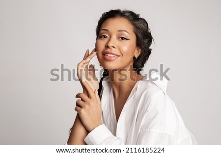 Beautiful mixed race young girl touch face enjoy perfect healthy smooth face skin, natural makeup. Pretty biracial female with ideal make-up posing on gray background. Skincare beauty cosmetics ad. Royalty-Free Stock Photo #2116185224