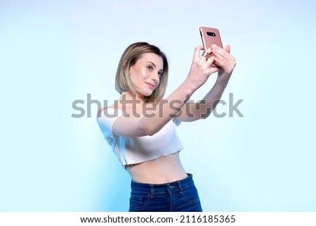 Photo of young caucasian girl with light blue eyes who takes selfie with her smartphone - Studio photography of pretty woman holding her phone photographing herself