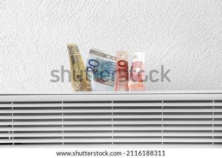 Euro banknotes on radiator near white wall. Concept of heating season