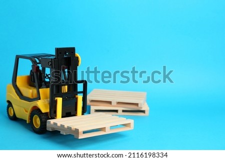 Toy forklift and wooden pallets on light blue background, space for text