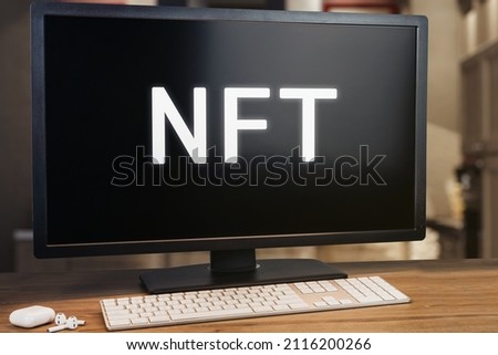 NFT on computer screen. Monitor, keyboard and earphone on wooden table. Selective focus.