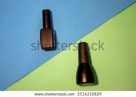 Black Bottles of Nail Polish on a Colorful Table. Bright and Shiny Nail Polish Bottles on Blue and Light Green Backgrounds. Manicure Tools, Beauty, Nail Art Concept. Selective Focus. 