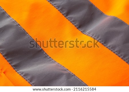 Orange signal vest with silver reflective stripes, background. Macro, equipment, warning