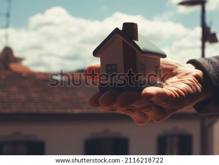 Italian real agent man holding a small house with a classic Italian house scenery as background . 