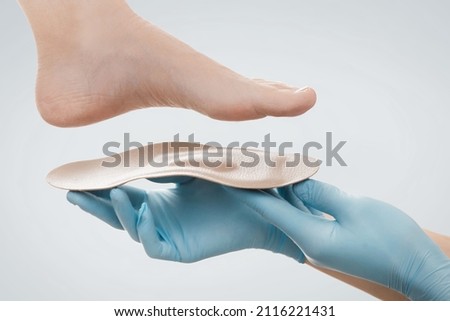 Orthopedic insole isolated on a white background. Hands in rubber gloves hold an orthopedic insole. Foot care, comfort for the feet. Doctor orthopedist tests the medical device. Flat feet correction. Royalty-Free Stock Photo #2116221431