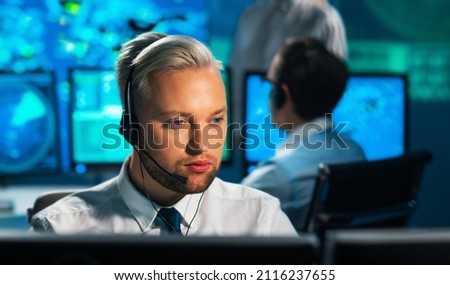 Aircraft flight control officer monitors the approach of aircraft from control tower. Air services office is equipped with navigation systems, radars and computer stations. Aviation concept. Royalty-Free Stock Photo #2116237655