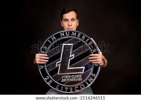 A man holds a litecoin coin in his hands as a symbol of technology. Image on black background