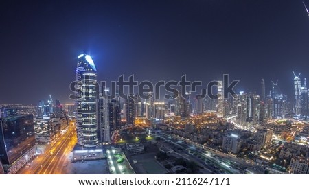 Panorama of Dubai's business bay and downtown towers during all night aerial timelapse. Rooftop view of some skyscrapers and new towers under construction and moon on the sky