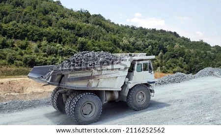 white Haul truck truck load of gravel rocks in the quarry from side view, big and large articulated dumping truck, dumper trailer, dump lorry. off-highway heavy-duty construction. Royalty-Free Stock Photo #2116252562